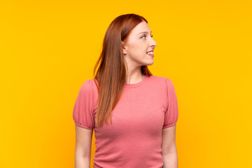 Young redhead woman over isolated yellow background looking to the side