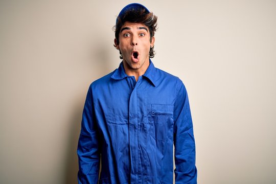 Young mechanic man wearing blue cap and uniform standing over isolated white background afraid and shocked with surprise expression, fear and excited face.