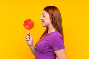 Young redhead woman holding a lollipop over yellow background