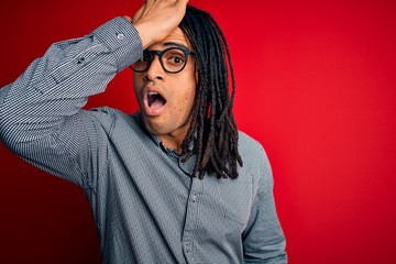 Young handsome african american man with dreadlocks wearing casual shirt and glasses surprised with...