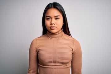 Fototapeta premium Young beautiful asian girl wearing casual turtleneck sweater standing over white background with serious expression on face. Simple and natural looking at the camera.