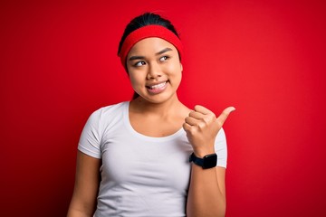Obraz na płótnie Canvas Young beautiful asian sporty woman wearing sportswear doing sport over red background smiling with happy face looking and pointing to the side with thumb up.