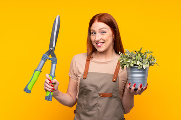 Young redhead gardener woman withpruning shears over isolated yellow background