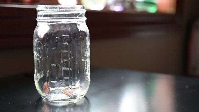 Slow motion of two fingers dropping coins into a glass jar