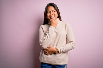 Young beautiful asian girl wearing casual turtleneck sweater over isolated pink background with hand on chin thinking about question, pensive expression. Smiling with thoughtful face. Doubt concept.