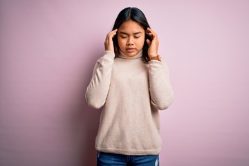 Young beautiful asian girl wearing casual turtleneck sweater over isolated pink background with hand on head for pain in head because stress. Suffering migraine.
