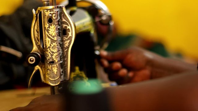 Ornately decorated antiques sewing machine being used by woman in Kenya to sew fabric. African woman making handmade clothing or crafts from cloth material. Golden light in tailor shop. SLIDE RIGHT.