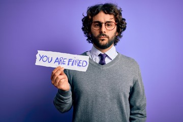 Handsome business man with beard holding you are fired message over purple background with a confident expression on smart face thinking serious