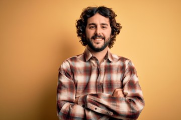 Young handsome man with beard wearing casual shirt standing over yellow background happy face smiling with crossed arms looking at the camera. Positive person.