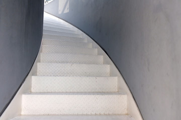 Spiral staircase in the building. Metal white steps leading up the corridor and gray walls.