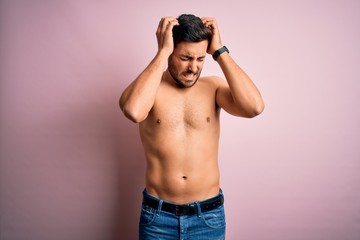 Fototapeta premium Young handsome strong man with beard shirtless standing over isolated pink background suffering from headache desperate and stressed because pain and migraine. Hands on head.