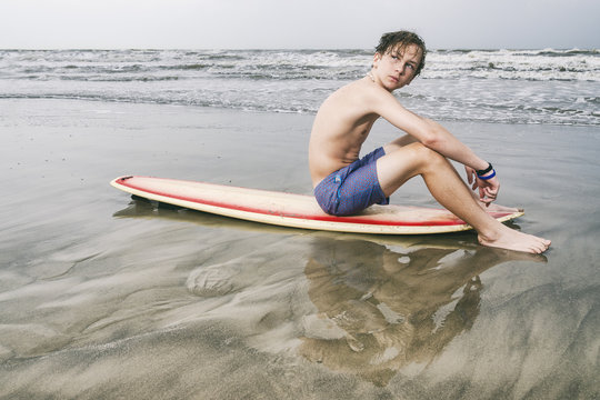 Young teen surfer sitting on surfboard at the Beach