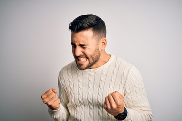 Young handsome man wearing casual sweater standing over isolated white background very happy and excited doing winner gesture with arms raised, smiling and screaming for success. Celebration concept.