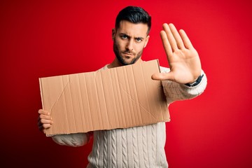 Young handsome man holding blank cardboard banner over isolated red background with open hand doing...