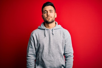 Young handsome sportsman wearing sweatshirt standing over isolated red background Relaxed with serious expression on face. Simple and natural looking at the camera.