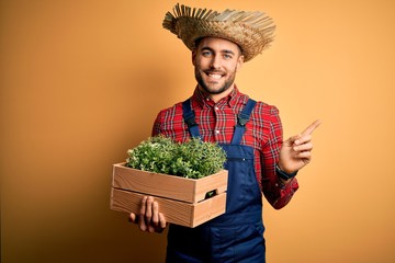 Young rural farmer man wearing countryside hat holding green organic plant from harvest very happy...