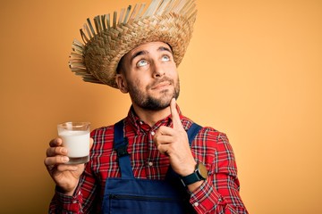 Young rural farmer man wearing countryside hat drinking organic milk from farm serious face...