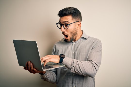 Young business man wearing glasses working using computer laptop scared in shock with a surprise face, afraid and excited with fear expression