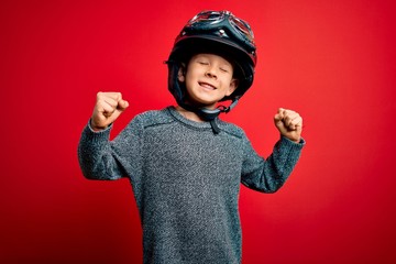 Young little caucasian kid wearing vintage biker motorcycle helmet and googles over red background...