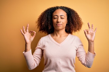 Young african american woman with afro hair wearing casual sweater over yellow background relax and smiling with eyes closed doing meditation gesture with fingers. Yoga concept.