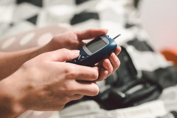 Theme diabetes. A close-up macro plan. Hands of a young Caucasian woman at home in the bedroom on the bed. It uses the technology of an instrument for measuring the level of glucose in the blood