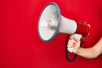 Beautiful hand of man holding megaphone over isolated red background