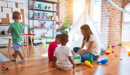 Young beautiful teacher and toddlers playing around lots of toys at kindergarten