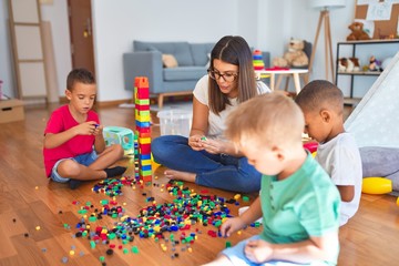 Young beautiful teacher and toddlers playing with building blocks around lots of toys at...