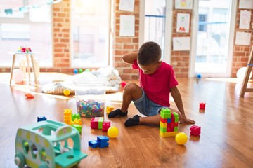 Adorable toddler playing with building blocks around lots of toys at kindergarten