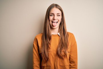 Young beautiful redhead woman wearing casual sweater over isolated white background sticking tongue out happy with funny expression. Emotion concept.