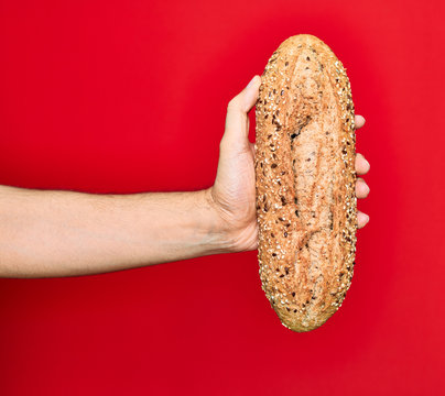 Beautiful hand of man holding wholemeal integral bread with cereals over isolated red background