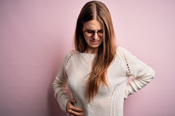 Young beautiful redhead woman wearing casual sweater and glasses over pink background Suffering of backache, touching back with hand, muscular pain