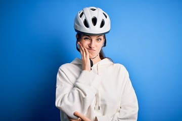 Young beautiful redhead cyclist woman wearing bike helmet over isolated blue background thinking...