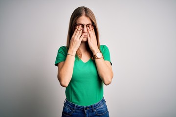 Young beautiful redhead woman wearing casual green t-shirt and glasses over white background rubbing eyes for fatigue and headache, sleepy and tired expression. Vision problem