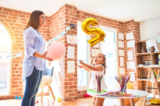 Caucasian girl kid playing and learning at playschool with female teacher. Mother and daughter at playroom playing with balloom