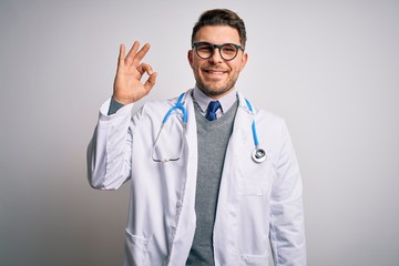 Young doctor man with blue eyes wearing medical coat and stethoscope over isolated background smiling positive doing ok sign with hand and fingers. Successful expression.
