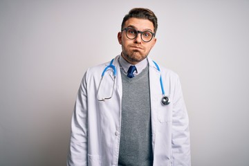 Young doctor man with blue eyes wearing medical coat and stethoscope over isolated background puffing cheeks with funny face. Mouth inflated with air, crazy expression.