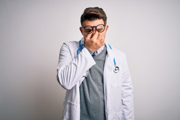 Young doctor man with blue eyes wearing medical coat and stethoscope over isolated background tired rubbing nose and eyes feeling fatigue and headache. Stress and frustration concept.