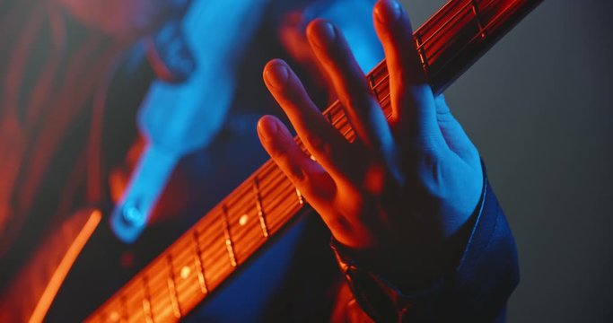 Close-up of bass player making a solo. An experienced musician starring on stage with rock music, lit by red and blue neon lights - music, hobby concept 4k footage