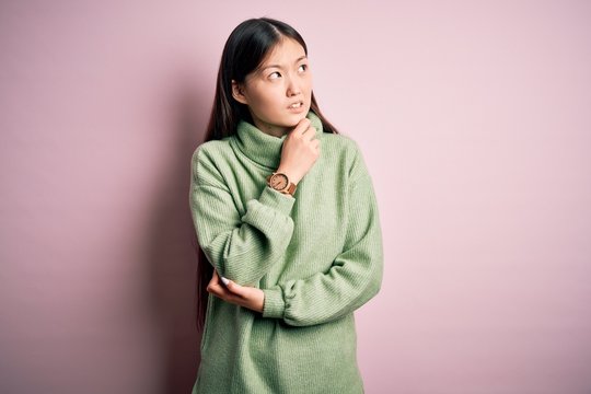 Young beautiful asian woman wearing green winter sweater over pink solated background Thinking worried about a question, concerned and nervous with hand on chin