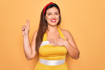 Young hispanic pin up woman wearing fashion sexy 50s style over yellow background smiling swearing...