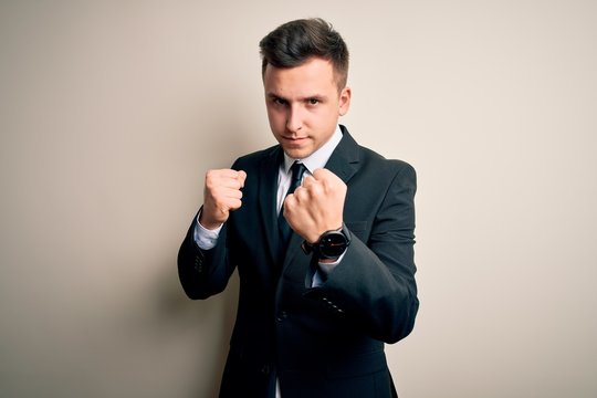 Young handsome business man wearing elegant suit and tie over isolated background Ready to fight with fist defense gesture, angry and upset face, afraid of problem
