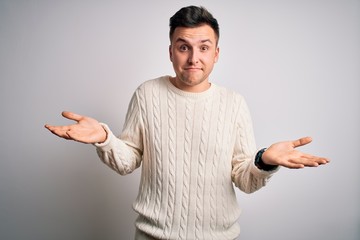 Fototapeta premium Young handsome caucasian man wearing casual winter sweater over white isolated background clueless and confused expression with arms and hands raised. Doubt concept.