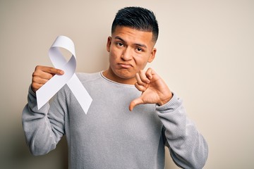 Young latin man holding white cancer ribbon supporting stop women violence with angry face, negative sign showing dislike with thumbs down, rejection concept