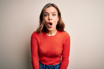 Young blonde girl wearing casual red sweater over isolated background afraid and shocked with surprise expression, fear and excited face.