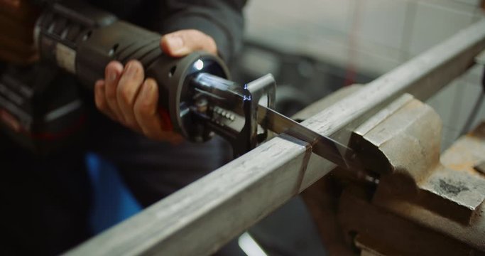 industry worker metal part with electric hacksaw