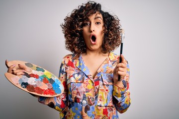 Young beautiful curly arab artist woman painting using brush and palette with colors scared in...