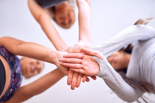 Young beautiful group of sportswomen standing shaking hands after class of yoga at gym