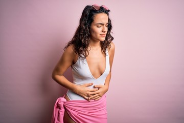Beautiful woman with curly hair on vacation wearing white swimsuit over pink background with hand on stomach because indigestion, painful illness feeling unwell. Ache concept.