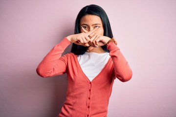 Young beautiful chinese woman wearing casual sweater over isolated pink background Rejection expression crossing fingers doing negative sign